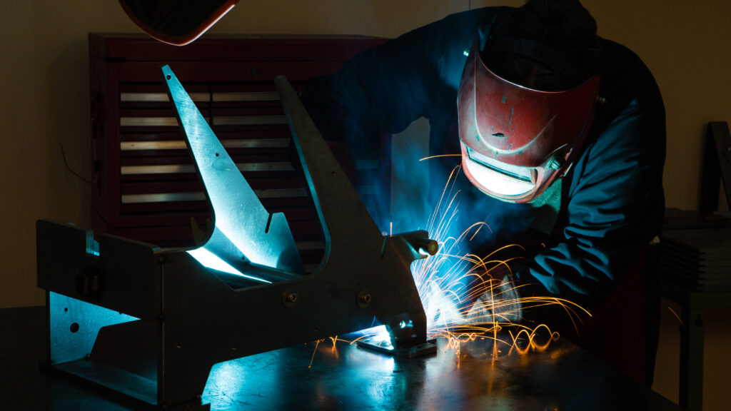 Dark image of a man wearing a mask and welding with sparks flying